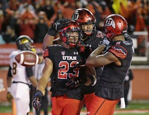 Utah running back Devontae Booker (23) receives a hug from teammates Sam Tevi (52) and Kenneth Scott (2) after scoring during the second half of an NCAA college football game against Arizona State on Saturday, Oct. 17, 2015, in Salt Lake City. Utah won 34-18. (AP Photo/Rick Bowmer)